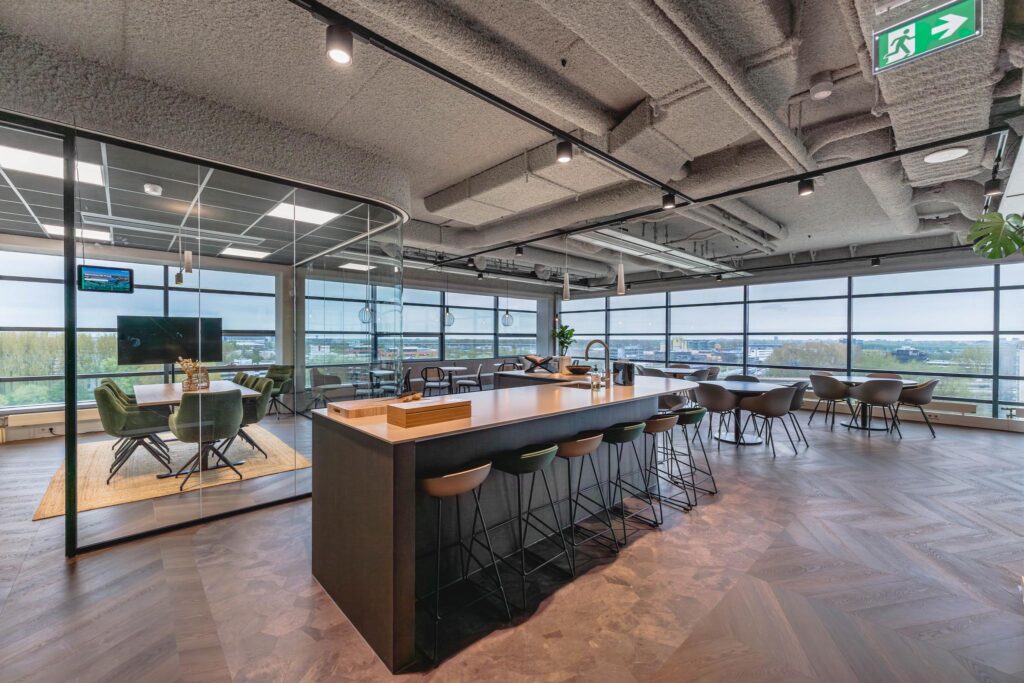 Modern open office space at Joop Geesinkweg with a kitchen island, seating area, and glass-walled meeting room.